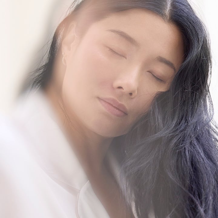 Femme &eacute;clair&eacute;e par une lumi&egrave;re douce, avec les yeux ferm&eacute;s et une expression sereine 